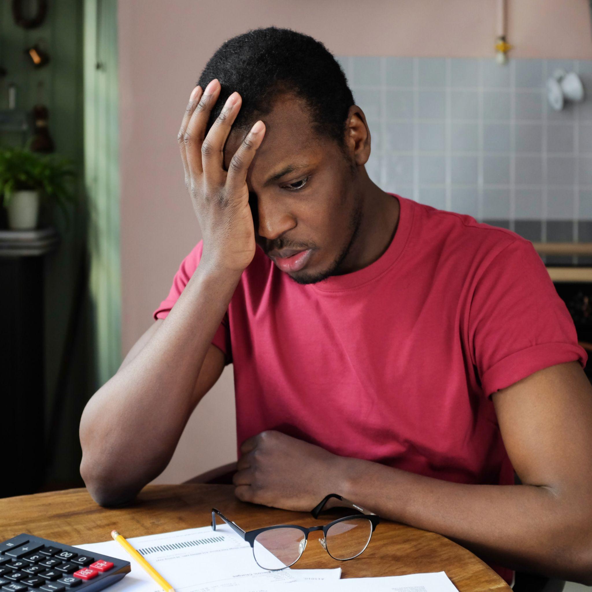 A guy overwhelmed with debts sitting at his desk with calculator and bills.